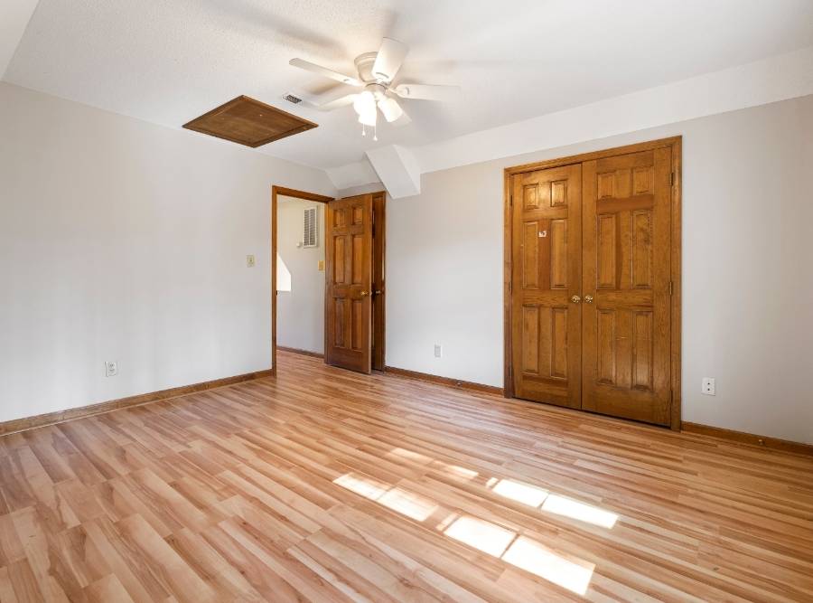 Empty room with polished hardwood flooring, white walls, ceiling fan, and wooden doors